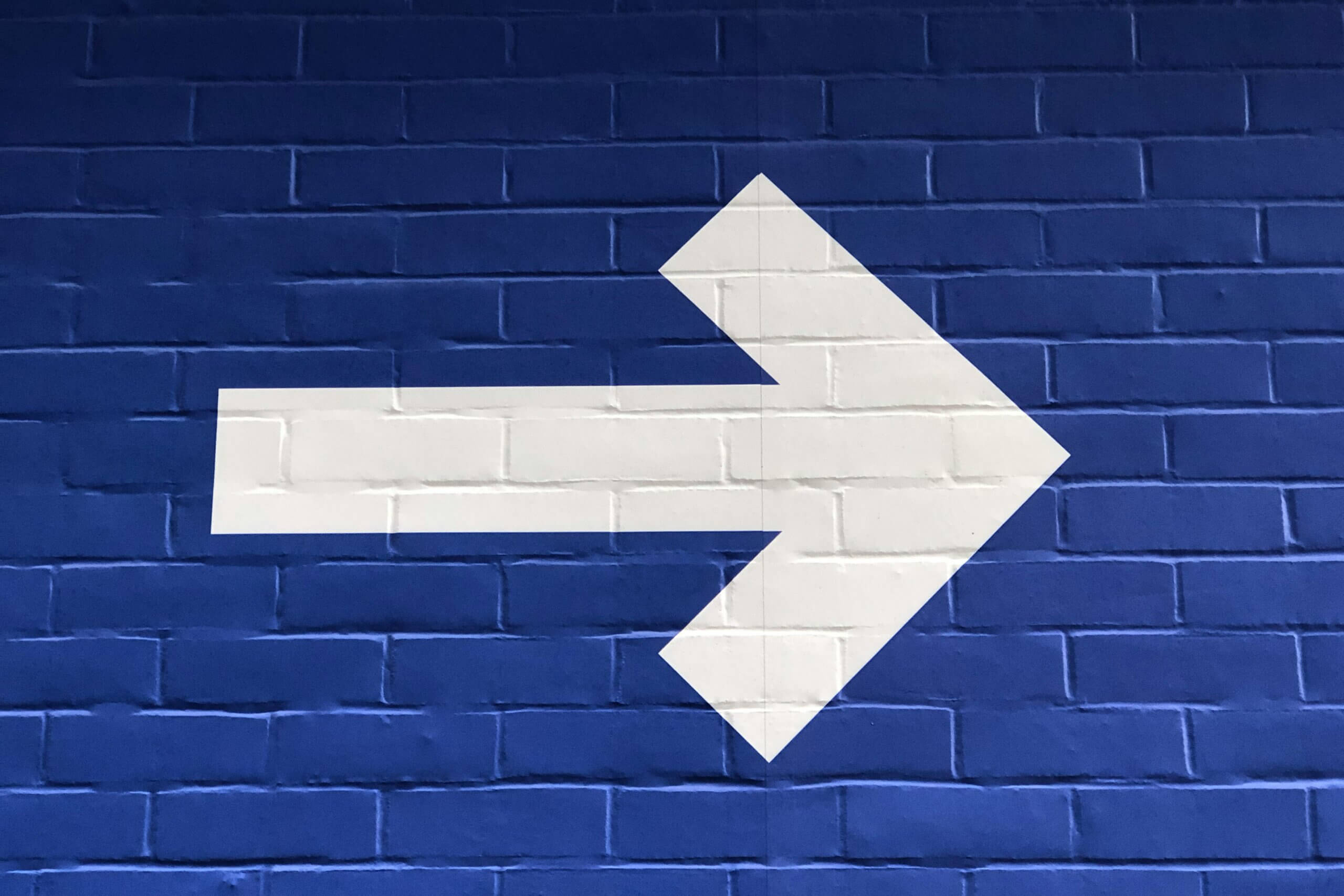 forward arrow, white, with bright blue brick background