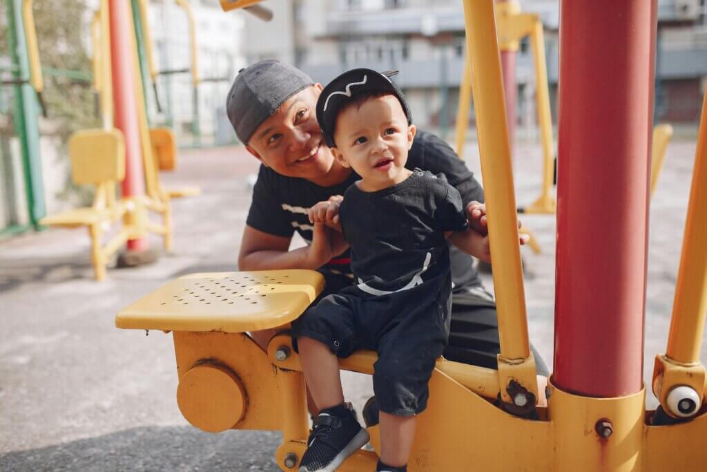 Father plays with his son at a playground. Smiles on both faces.