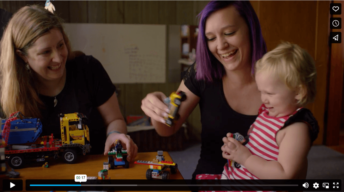 Mom, baby and home visitor all laugh together while sitting at a table.