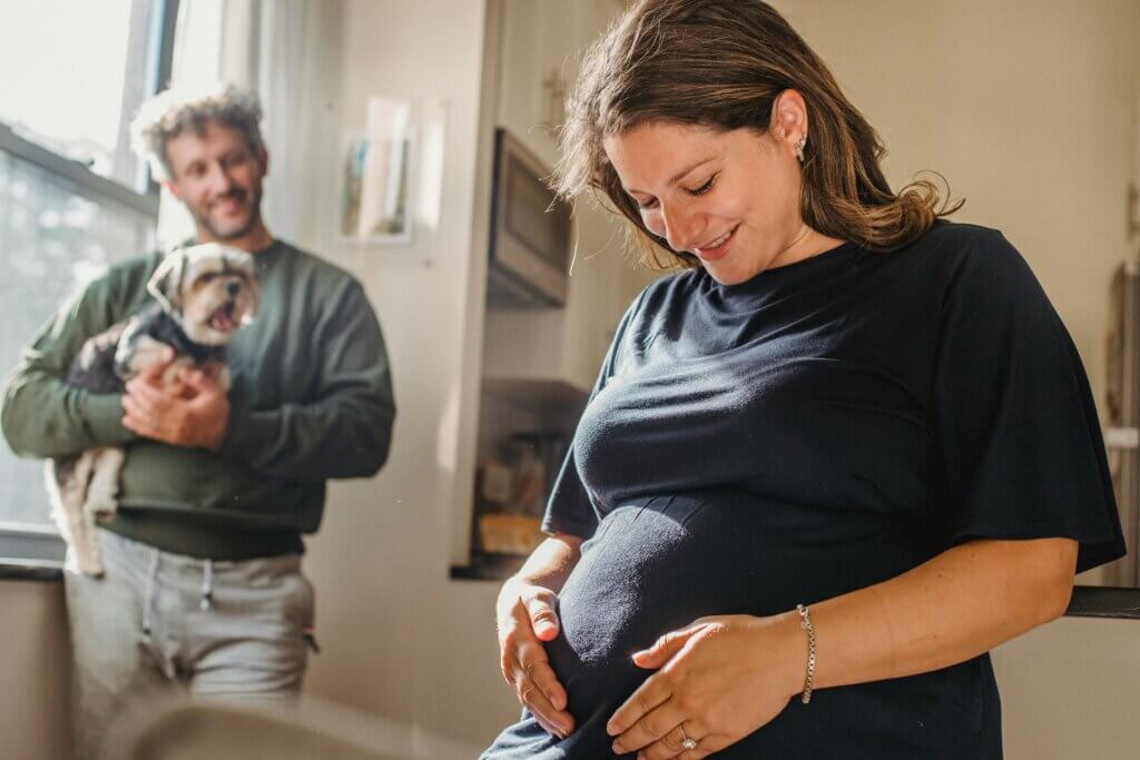 Woman holds her pregnant belly while another looks on with pride