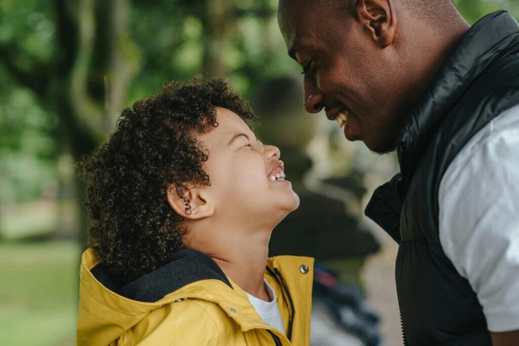 Little boy with curly hairs looks up, smiling wide at his father who smiles back