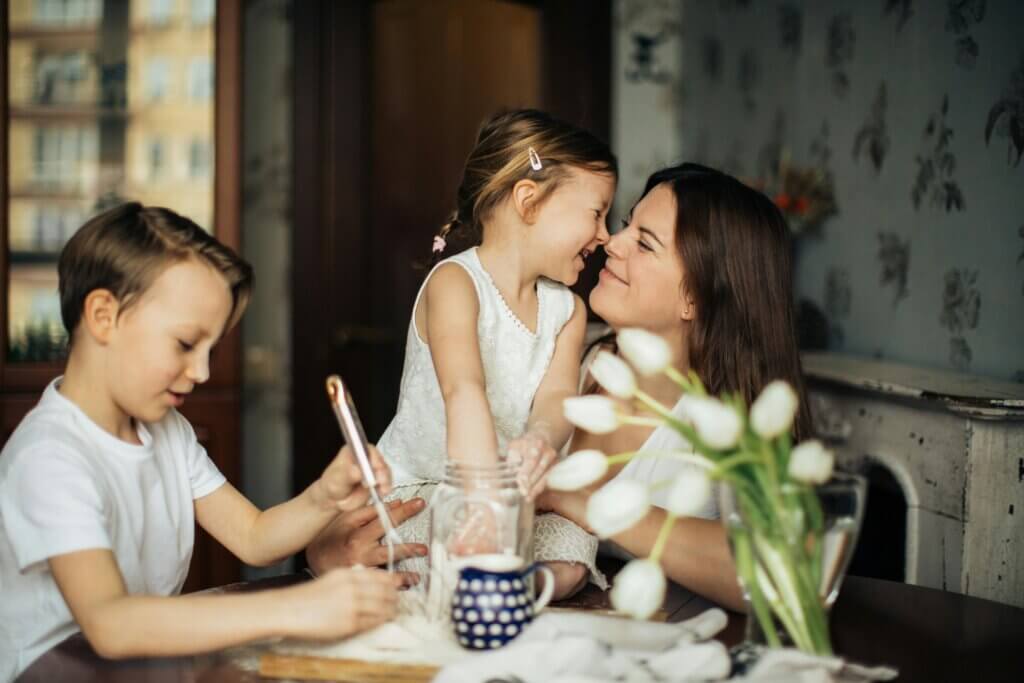 Mom nuzzles noses with daughter, brother pains next to them at the table