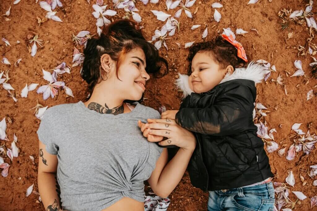 Mom and daughter look lovingly at each other while laying on the floor facing up towards the ceiling