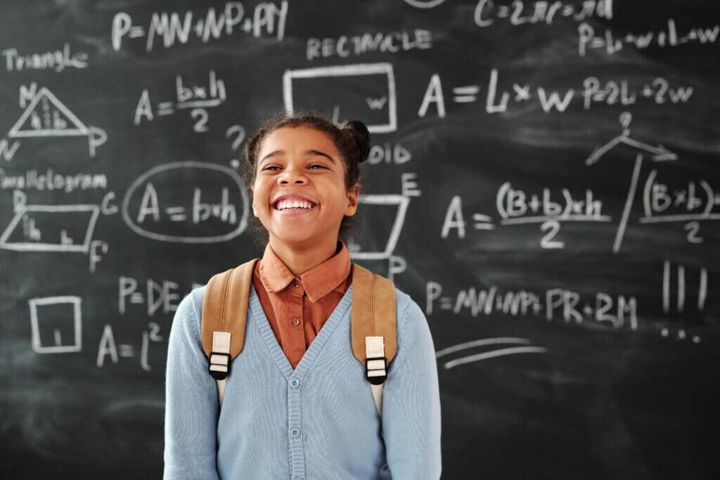 Proud student stands in front of complex equations on the blackboard