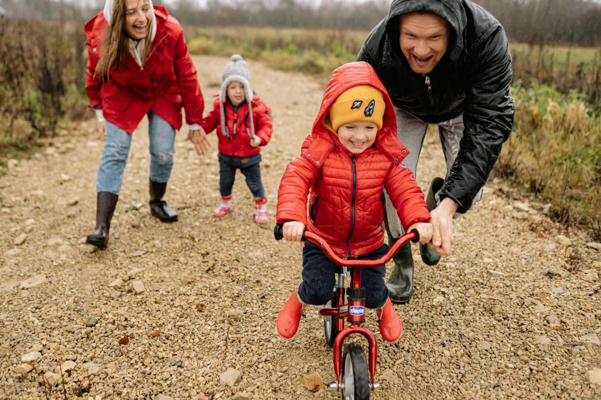 Little boy on bicycle moves forward with the support of his Dad, directly behind him. A proud mother and sister follow along closely too